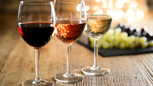 three glass of white red and rose wine with dim light in wooden restaurant table with a grape background